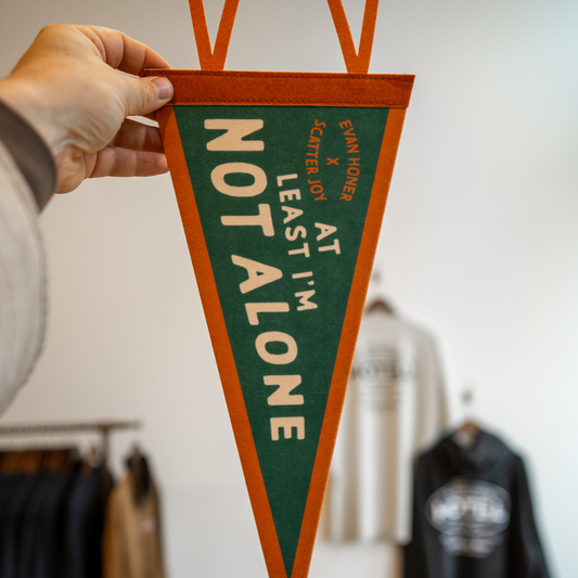 Hand holding a green and orange pennant with text in a clothing store setting